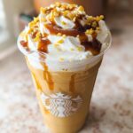 A close-up of a homemade Caramel Ribbon Crunch Frap Copycat topped with whipped cream, caramel drizzle, and crunchy topping.