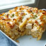 A close-up serving of baked Chicken Alfredo Casserole showing penne pasta, chunks of chicken, and a bubbly, browned cheese topping.