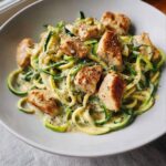 Close-up of Chicken Alfredo with Zucchini Noodles coated in creamy sauce and topped with cracked black pepper.