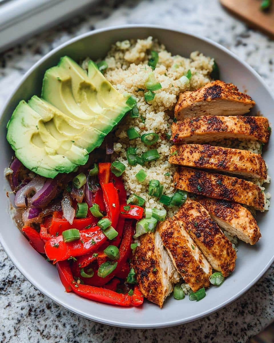 A vibrant Chicken Cauliflower Rice Bowl featuring sliced seasoned chicken, avocado, peppers, and onions over cauliflower rice.