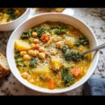 Close-up of a hearty bowl of Chickpea Vegetable Soup, featuring chickpeas, potatoes, kale, and carrots, topped with pepper.