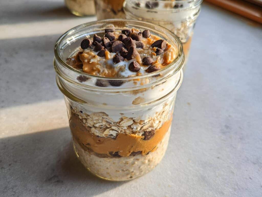 Close-up of Chocolate Chip Cookie Dough Overnight Oats layered in a mason jar, topped with peanut butter and chips.