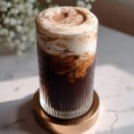 A tall glass of Chocolate Cream Cold Brew Copycat topped with thick cream and cocoa powder.