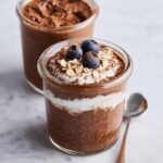 Close-up of Chocolate Protein Overnight Oats layered with yogurt, topped with blueberries and oats.