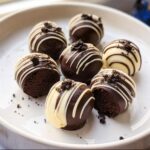 Seven decadent Classic No-Bake Oreo Balls, half dipped in dark chocolate with white drizzle, served on a white plate.