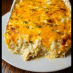 A scoop taken from a baked Creamy Chicken and Rice Casserole topped with melted cheddar cheese and parsley.