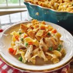 A serving of creamy Chicken Noodle Casserole featuring egg noodles, shredded chicken, peas, carrots, and topped with crunchy croutons.