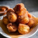 A tempting pile of golden brown Crispy Air Fryer Churro Bites heavily coated in cinnamon sugar, served on a white plate.