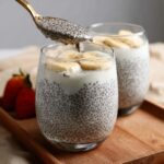 A spoonful of creamy Dairy-Free Vanilla Chia Pudding is being lifted from a glass topped with banana slices.