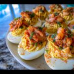 Close-up of several Delightful Crawfish Deviled Eggs topped with seasoned crawfish and paprika on a serving platter.