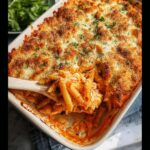 A wooden spoon scooping out a serving of creamy Dump-and-Bake Chicken Parmesan Casserole with a golden, crispy topping.