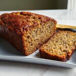 A freshly baked loaf of Easiest Homemade Banana Bread, partially sliced on a white platter.