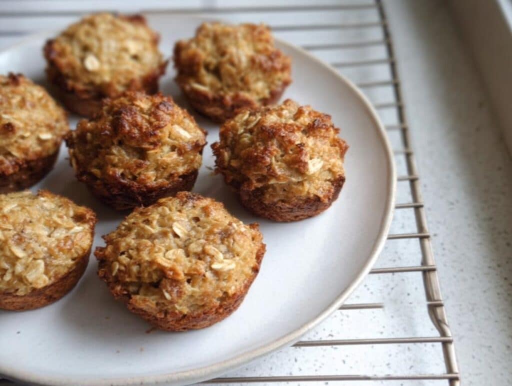 A plate holding several golden-brown Easy Banana Oat Snack Bites, cooling on a wire rack.