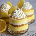 Close-up of Easy Lemon Dessert Cups layered with lemon filling, graham cracker crust, and topped with whipped cream and a lemon slice.