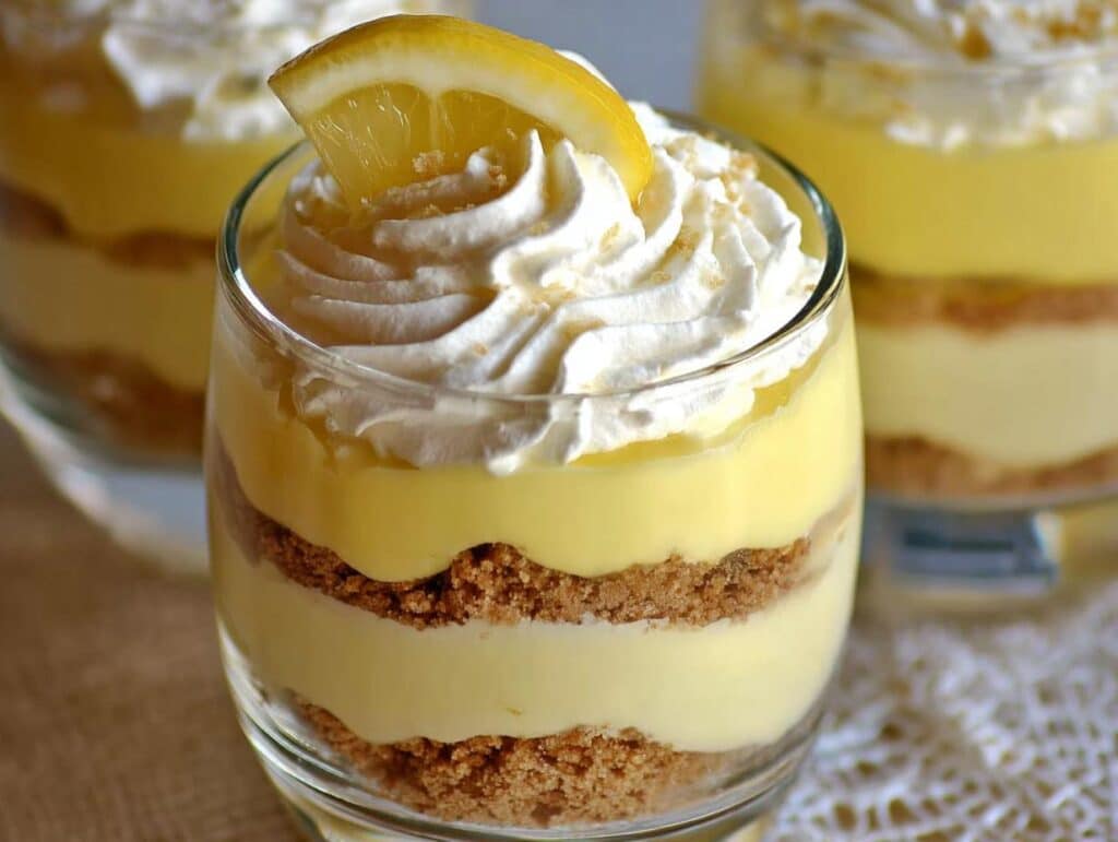 Close-up of one of the Easy Lemon Dessert Cups layered with graham cracker crust, lemon filling, and topped with whipped cream and a lemon slice.