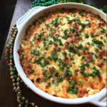 A bubbling, cheesy Easy Mardi Gras Hot Muffuletta Dip topped with fresh parsley in a white baking dish.