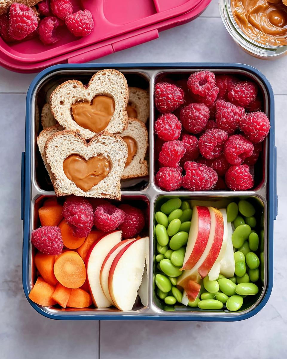 A bento box featuring heart-shaped peanut butter sandwiches, raspberries, carrots, apples, and edamame for an Easy Valentine Lunch Bento for Kids.