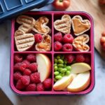 Overhead view of an Easy Valentine Lunch Bento for Kids featuring heart-shaped toast with peanut butter, raspberries, apple slices, and edamame.
