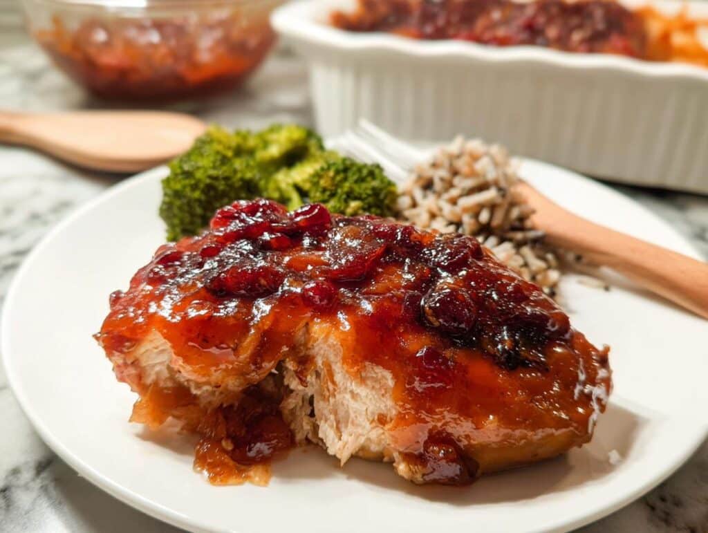 Close-up of a serving of Fall Chicken Casserole with Cranberry Notes, topped with a thick cranberry glaze, served with rice and broccoli.