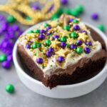 A square of rich chocolate Fat Tuesday Sprinkle Brownies topped with white frosting and Mardi Gras colored sprinkles and gold stars.