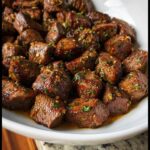 Close-up of juicy Garlic Butter Steak Bites coated in glistening garlic and parsley sauce in a white bowl.