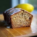 Cross-section of moist Lemon Banana Bread drizzled with white glaze, with a lemon in the background.