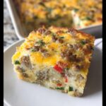 A thick slice of Gluten-Free Breakfast Casserole topped with melted cheese and sausage on a white plate.