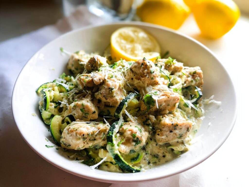 Close-up of Gluten-Free Chicken Alfredo served with zucchini noodles, topped with Parmesan cheese and a lemon slice.