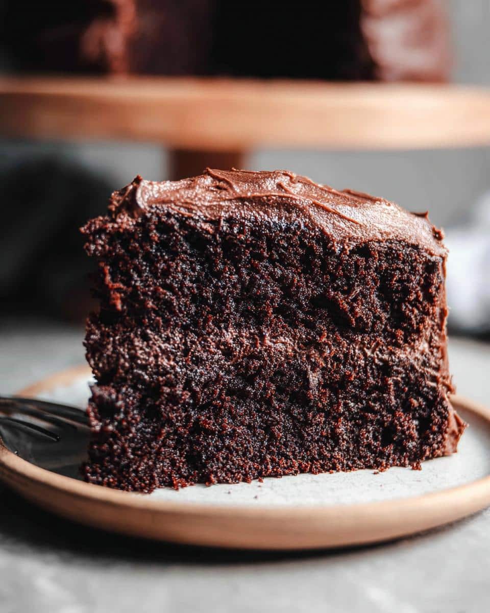 Close-up of a moist slice of Gluten-Free Dairy-Free Chocolate Cake topped with rich chocolate frosting.