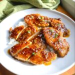 Slices of glossy, glazed Gluten-Free Honey Garlic Chicken served over white rice, garnished with sesame seeds.