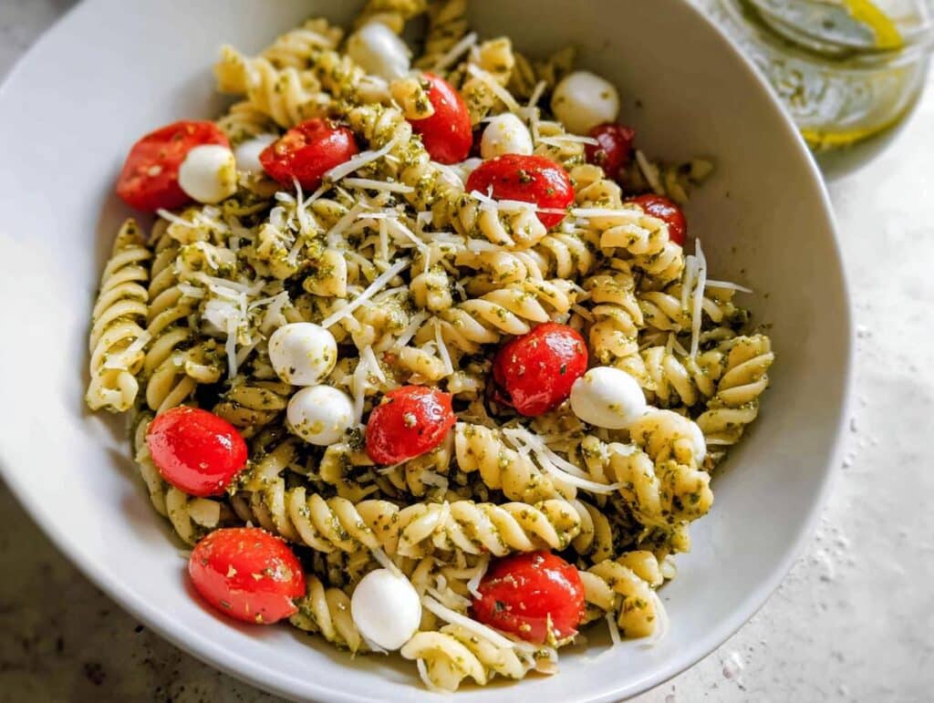 Close-up of a Gluten-Free Pesto Pasta Bowl featuring fusilli pasta, cherry tomatoes, mozzarella balls, and grated cheese.