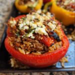 A close-up of a vibrant red Gluten-Free Stuffed Bell Pepper filled with seasoned ground meat, rice, and topped with crumbled feta cheese.