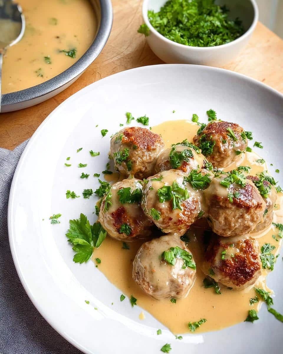 A white plate featuring several browned Gluten-Free Swedish Meatballs covered in creamy gravy and topped with fresh parsley.