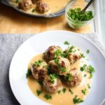 Five Gluten-Free Swedish Meatballs served on a white plate with creamy gravy and fresh parsley garnish.