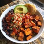 A vibrant Gluten-Free Sweet Potato Black Bean Bowl featuring roasted sweet potatoes, black beans, brown rice, avocado, and hot sauce.