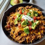 Close-up of a Gluten-Free Taco Skillet topped with avocado, tomato, sour cream, and cilantro in a black pan.