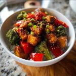 Close-up of a Gluten-Free Teriyaki Chicken Bowl featuring glazed chicken pieces, bright red peppers, and broccoli florets over rice.