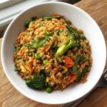 A close-up of a white bowl filled with savory Gluten-Free Vegetable Fried Rice, featuring broccoli, peas, carrots, and snow peas.