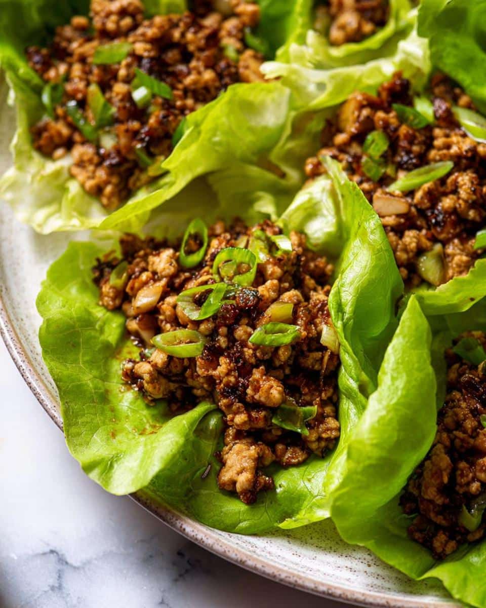 Close-up of several vibrant Ground Chicken Lettuce Wraps filled with savory brown meat mixture and topped with green onions.