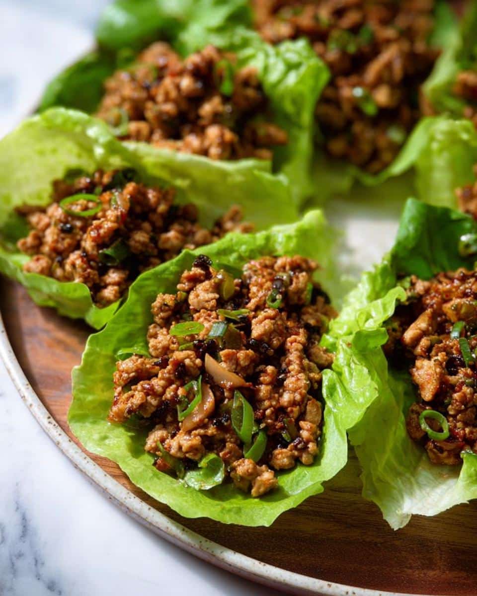 Close-up of several fresh Ground Chicken Lettuce Wraps filled with savory, browned ground chicken mixture and green onions.