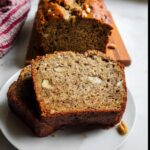 Two thick slices of moist Healthy Banana Bread with Whole Wheat featuring visible walnuts on a white plate.