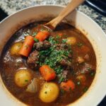 A close-up overhead view of a bowl of rich, dark Healthy Beef Stew, featuring chunks of beef, carrots, and small potatoes, garnished with parsley.