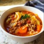 A close-up of a white bowl filled with Healthy Cabbage Roll Soup, featuring ground beef, cabbage, carrots, and tomato broth.