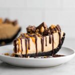 A decadent slice of Healthy Vegan Peanut Butter Pie with a dark crust, topped with chocolate and caramel drizzles and peanut butter cups.