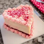 A close-up of a heart-shaped cake slice featuring pink frosting borders and red sprinkles, illustrating Cake Pop Heart Designs.