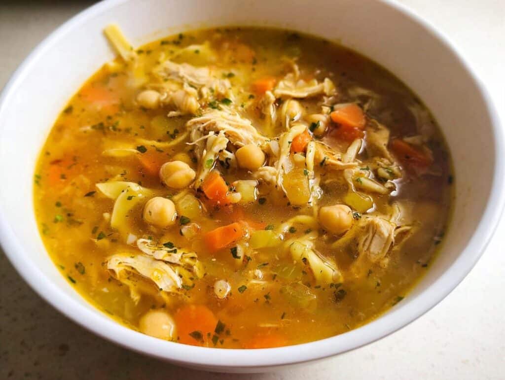 Close-up of a hearty bowl of High Protein Chicken Vegetable Soup featuring shredded chicken, carrots, chickpeas, and noodles.