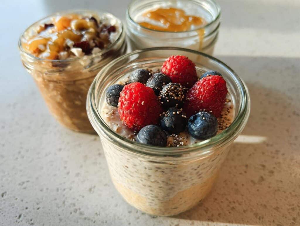 Three jars of High-Protein Overnight Oats, one topped with berries and chia seeds, ready for breakfast.