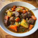 Close-up of a white bowl filled with rich Homestyle Beef Stew, featuring chunks of beef, potatoes, and carrots.