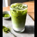 Tall glass showing layers of milk and bright green Iced Matcha Latte Starbucks Style with ice cubes.
