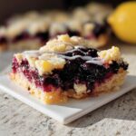 A close-up of a single serving of Lemon Blueberry Gluten-Free Bars, showing the thick blueberry filling and crumb topping with white glaze.